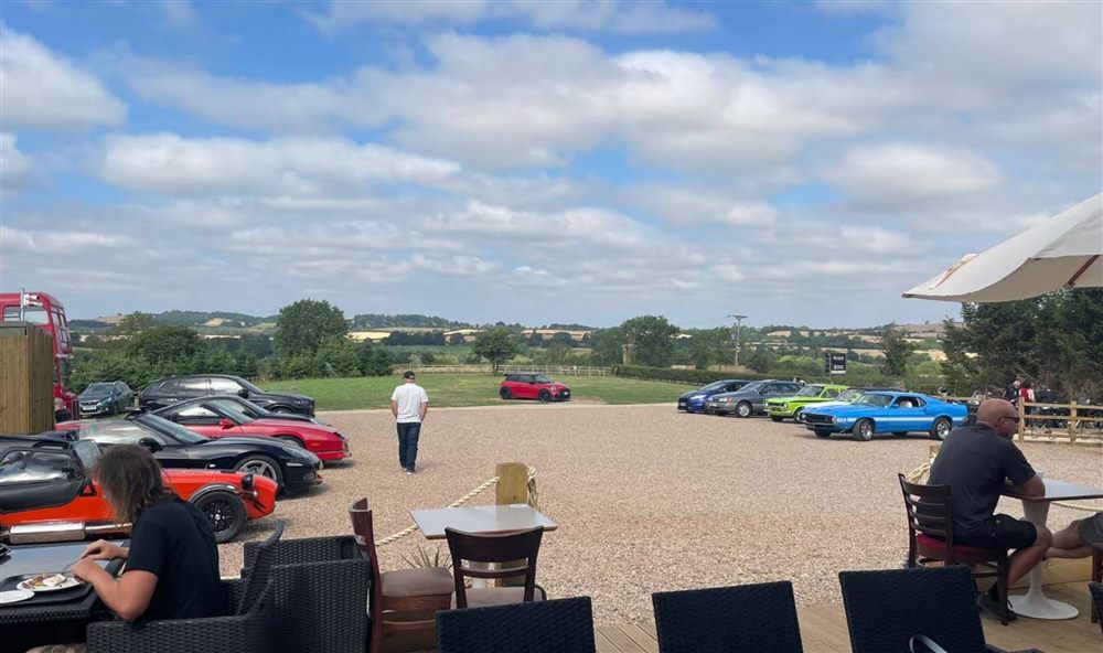 The car park at Pistons & Rings, filled with classic and sports cars, overlooking the Northamptonshire countryside